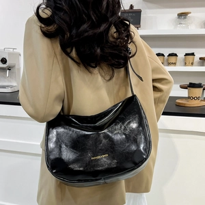 Fashion black crescent shoulder bag with gold lettering shown in a stylish cafe setting