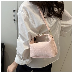 Detail shot of light pink snakeskin textured crossbody bag with golden hardware on a model