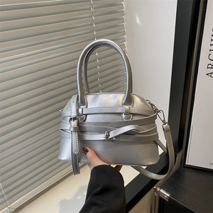 Sac à main argenté en forme de coquille avec sangles à boucles porté à la main