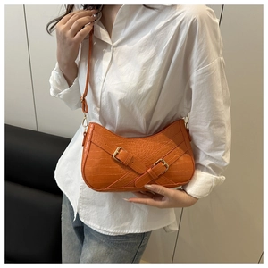 Detail of orange faux-crocodile shoulder bag with gold buckles on a minimalist background