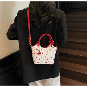 Détail du sac seau rétro à imprimé cerise avec poignées rouges et pendentif cerise