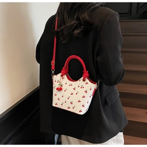 Détail du sac seau en cuir blanc avec motif cerise et bandoulière rouge porté par un mannequin