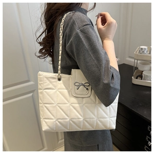 Detail of white quilted tote bag featuring silver metal bow buckle and chain strap