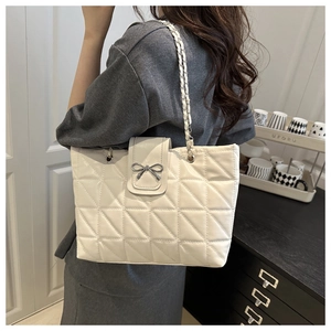 Close-up of white quilted tote bag with bow detail and chain strap on a model