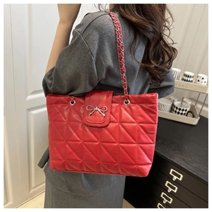 Detail of red quilted tote bag with metallic bow buckle and chain shoulder strap