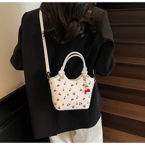 Détail du sac seau blanc à imprimé cerise porté par un mannequin sur un escalier