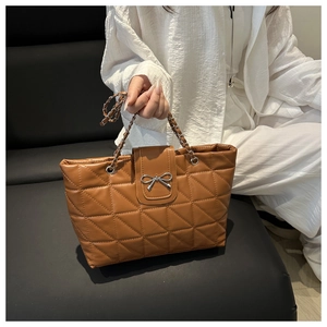 Detail of brown quilted tote bag featuring silver bow buckle and leather chain strap