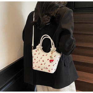 Détail du sac blanc à imprimé cerise avec poignées tressées porté par un mannequin