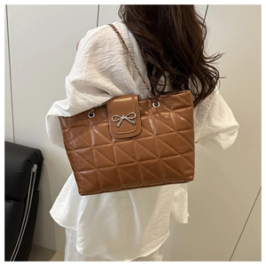 Quilted brown tote bag with silver bow accent and chain strap worn by a model