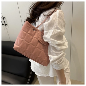 Side view of a pink quilted tote bag with chain strap worn by a model in a minimal setting