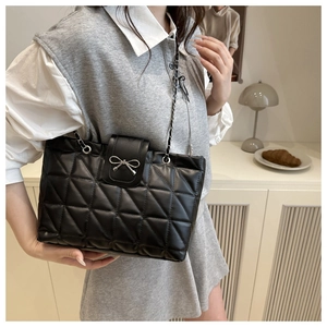 Close-up of black quilted shoulder bag with a silver metal bow and chain strap detail