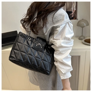 Close-up of black quilted shoulder bag with silver bow buckle and chain strap on model