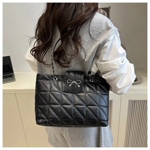 Detail of black quilted tote bag with silver bow clasp and metal chain shoulder strap