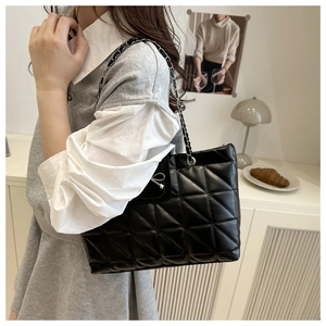 Modèle portant un sac cabas noir matelassé avec chaîne argentée et nœud en métal
