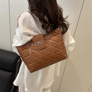Brown quilted tote bag with silver bow buckle and chain strap shown on a model