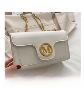 Detail of white leather crossbody bag featuring a golden M-logo and fine chain strap