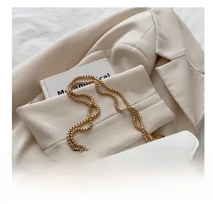 Detailed view of white crossbody bag with gold chain strap and M logo on a beige blazer