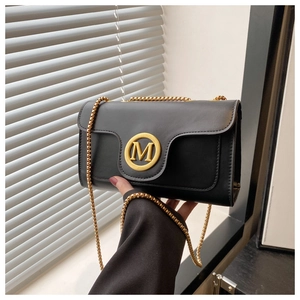 Detail of black leather flap crossbody bag with gold M buckle and chain strap