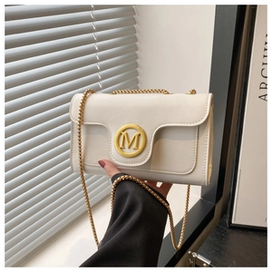 Close-up of cream crossbody bag featuring a golden M buckle and metal chain strap
