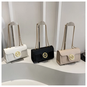 Close-up of three stylish flap square bags with gold M logo in white, black and beige