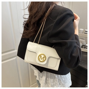 Detail of white leather crossbody bag with gold M buckle and chain strap on a black blazer