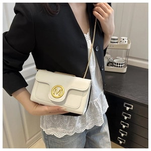 Detailed close-up of white crossbody bag featuring a golden M logo and metal chain strap