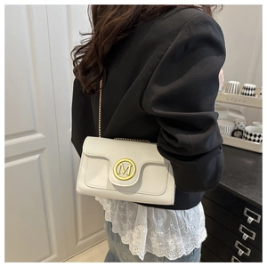 Close-up of white crossbody flap bag with gold M logo and chain strap on a model