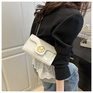 Close-up of white leather flap bag with gold M-logo buckle and elegant metal chain strap
