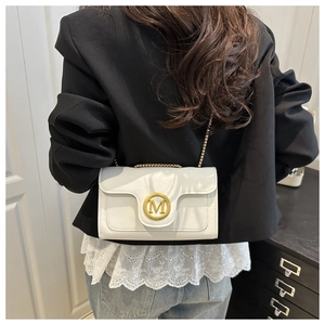 Close-up of white leather crossbody bag with golden M buckle on a model in black suit