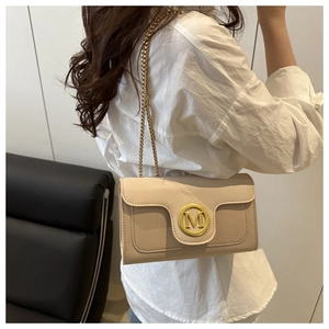 Detail of cream crossbody bag with golden M logo and elegant chain strap on model