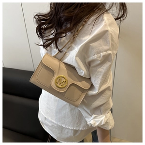 Detail view of a beige leather flap bag with golden M logo and chain strap on a model
