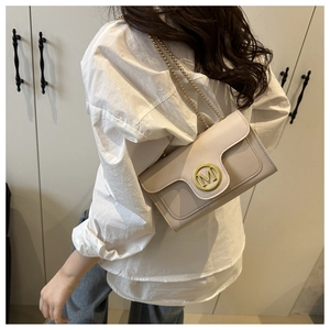 Detail of elegant beige crossbody bag with gold M-logo and fine chain strap worn by model