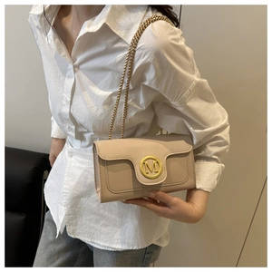 Close-up of beige crossbody bag with gold chain strap and letter M emblem on flap