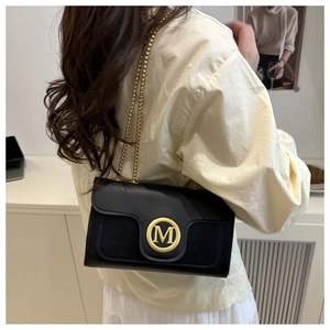 Macro detail of black quilted leather crossbody bag with gold M logo and chain strap