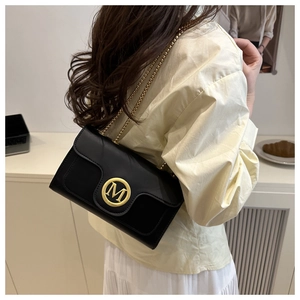 Detail of minimalist black leather crossbody bag with gold chain and M letter buckle