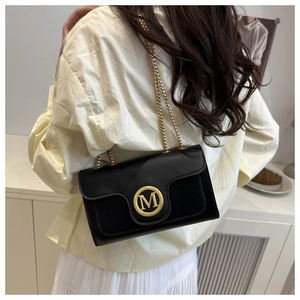 Detail of a black leather crossbody bag with a gold metal M-logo and chain strap