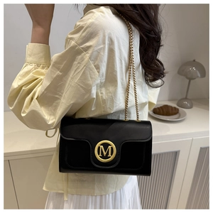 Detail of elegant black quilted crossbody bag featuring a golden M-shaped metal buckle clasp