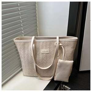 Detail of woven straw tote bag with gold logo plate and matching small zipper pouch