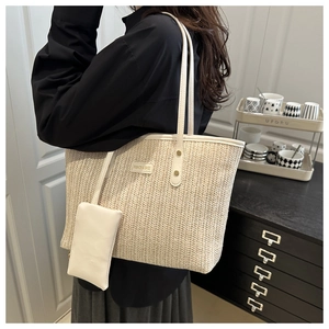 Detail of a woven straw tote bag featuring a leather brand tag and small matching pouch