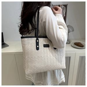 Close-up of woven straw tote bag with black leather trim and gold rivet details