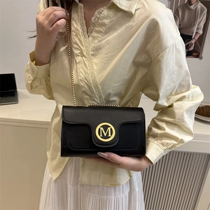 Women's black quilted crossbody bag with gold M logo and chain strap on casual outfit