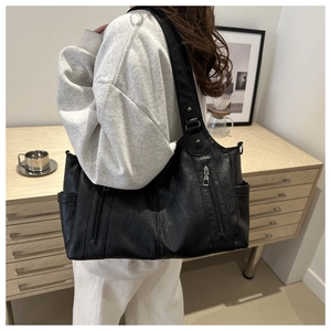 Detail of a large black tote bag with vertical zippers shown on a white outfit