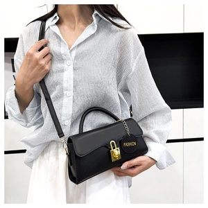 Detail of minimalist black leather crossbody bag with gold lock and fashion chain charm