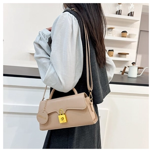 Detail shot of the beige leather shoulder bag with a gold buckle worn by a model in a cafe