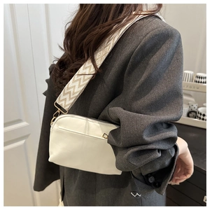 Detailed view of white crossbody bag with wide herringbone woven strap on grey blazer