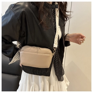 Detail of beige crossbody bag with a wide geometric patterned shoulder strap and gold hardware