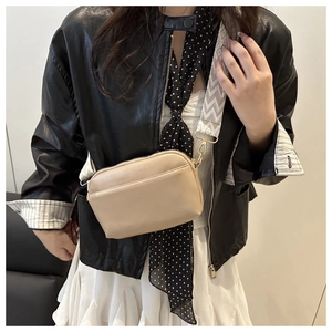 Vue détaillée du sac à bandoulière en cuir beige avec une large sangle ondulée