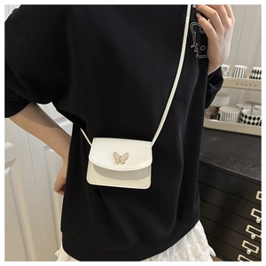 Close-up of a white mini crossbody bag with a butterfly clasp on a black sweatshirt
