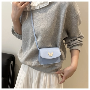 Detailed view of light blue mini bag with a golden butterfly charm and slim leather strap