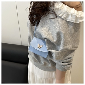 Detail of light blue mini crossbody bag with golden butterfly buckle worn by model